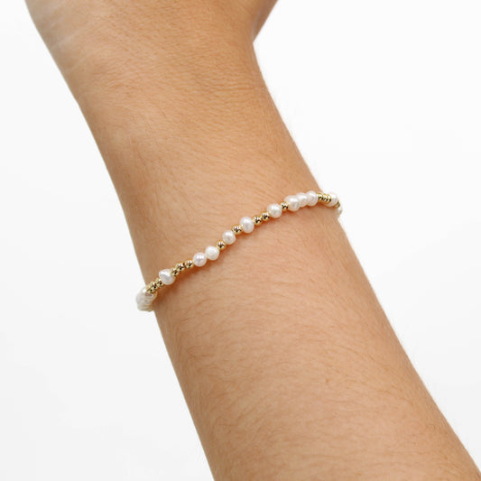 Gold pearl bracelet on a person's wrist against a white background