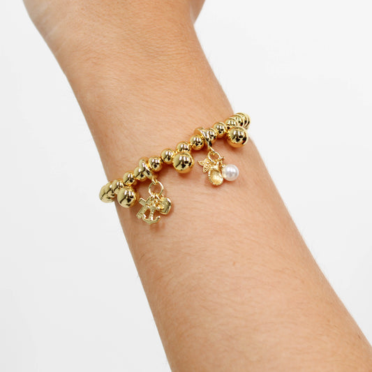 Gold bracelet with nautical charms on a wrist against a white background