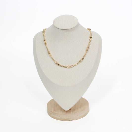 Gold necklace on a white bust with a wooden base against a white background