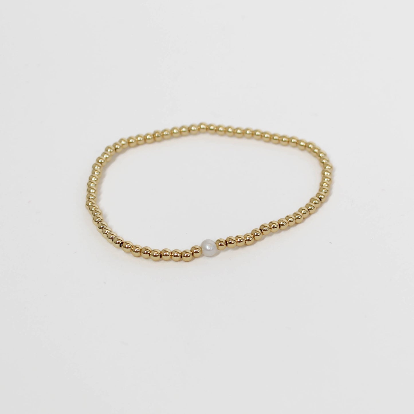 Gold beaded bracelet with a pearl on a light gray background