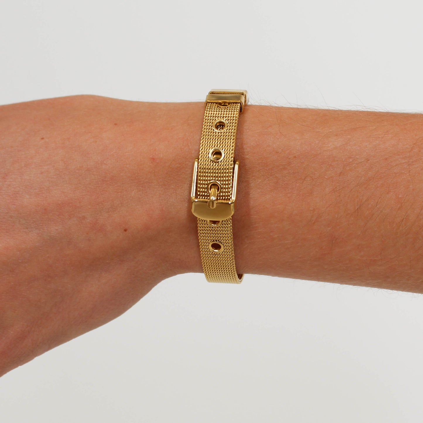 Gold belt bracelet on a wrist against a plain background