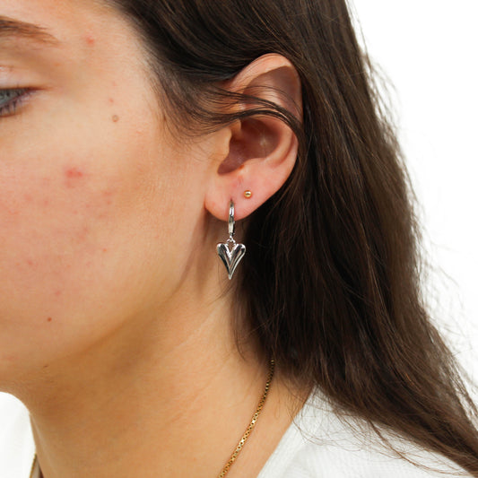 Close-up of a person wearing a silver heart-shaped bubble heart huggie earring.