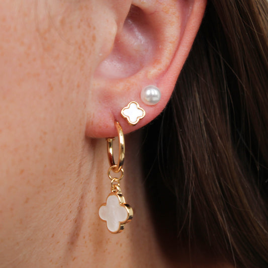 Close-up of an ear wearing a gold clover earring set in pink.