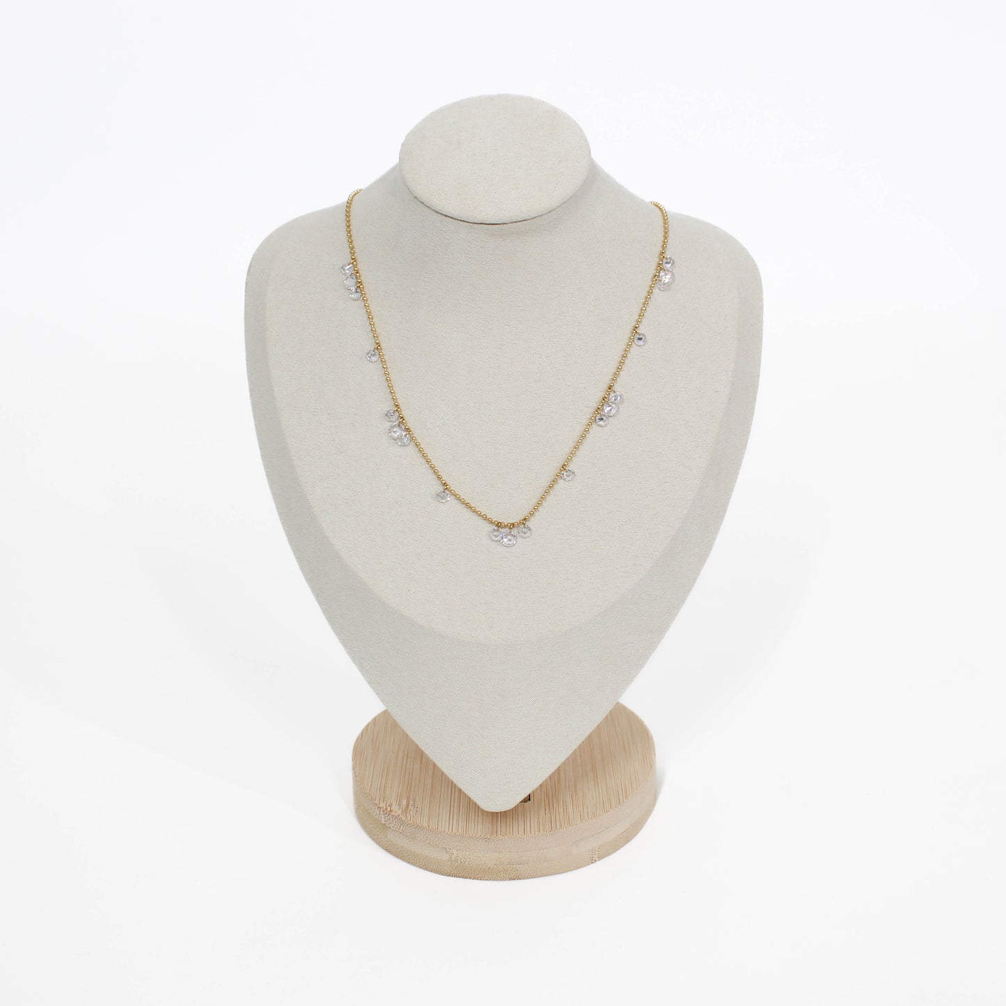 Gold drop crystal necklace on a white mannequin bust with a wooden base against a white background