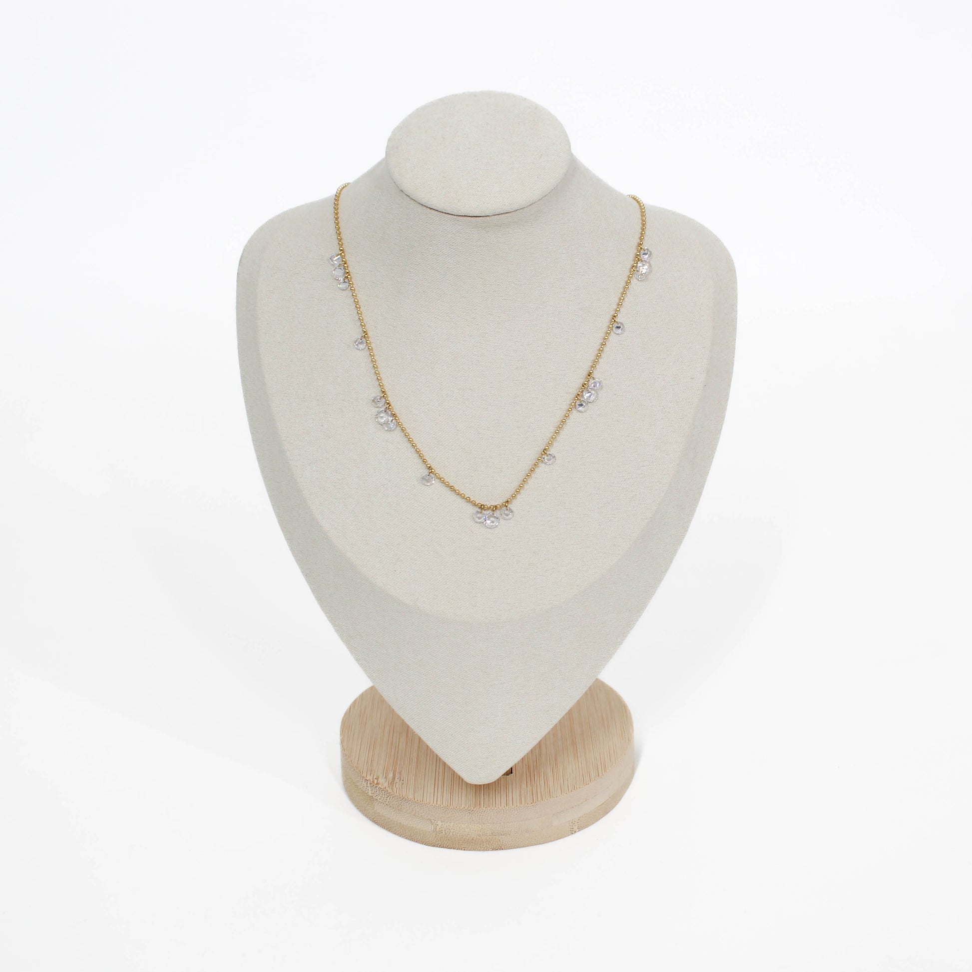 Gold drop crystal necklace on a white mannequin bust with a wooden base against a white background
