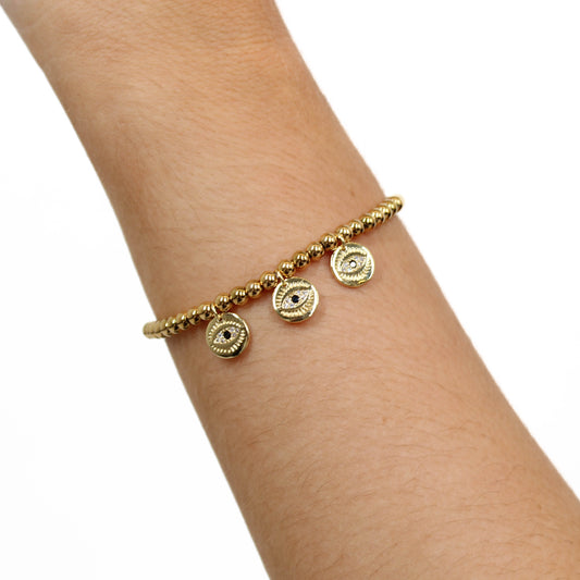 Gold bracelet with circular evil eye charms on a wrist against a white background
