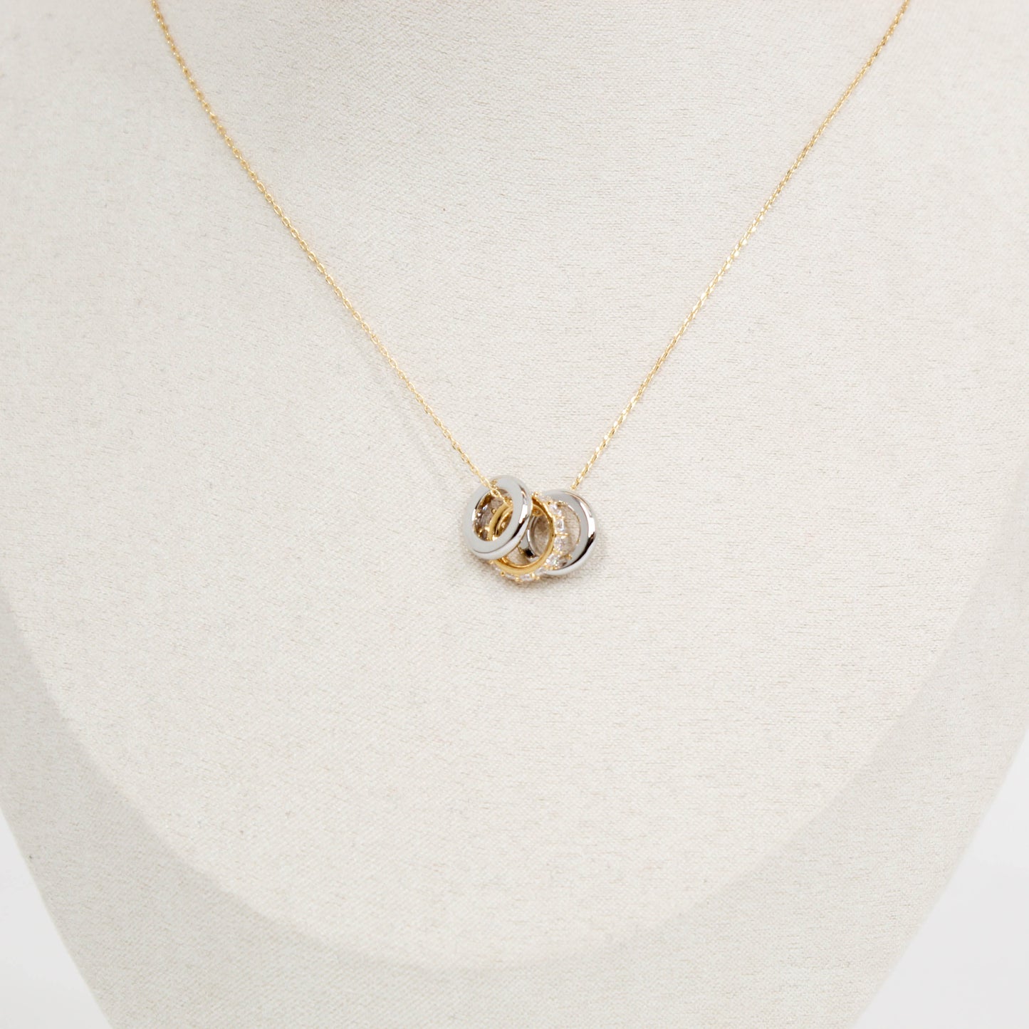 Gold necklace with a three ring pendant on a light beige background