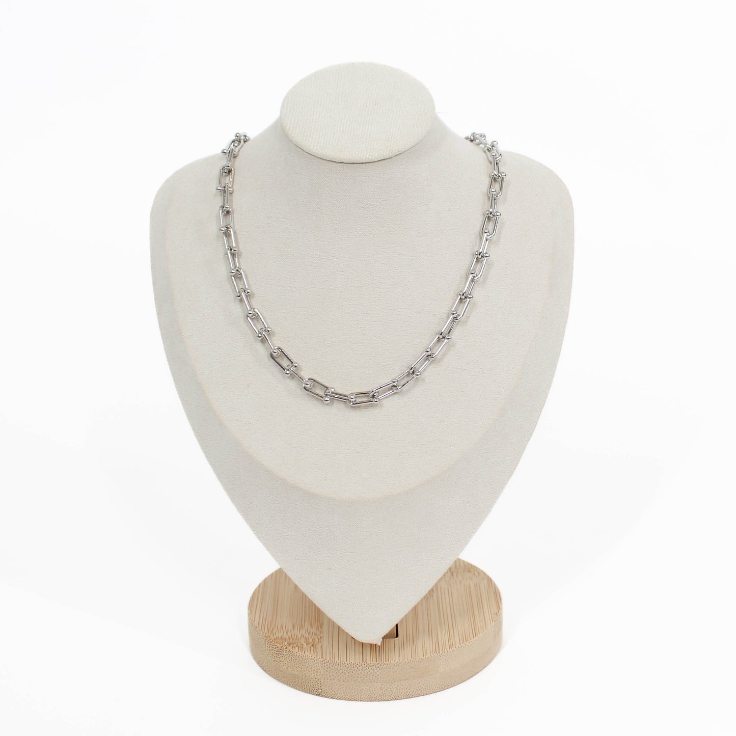 Silver chain hardware necklace on a white mannequin bust with a wooden base against a white background
