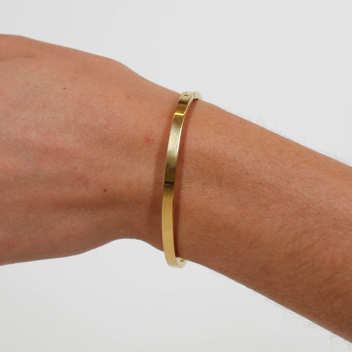 Gold bracelet on a wrist against a white background