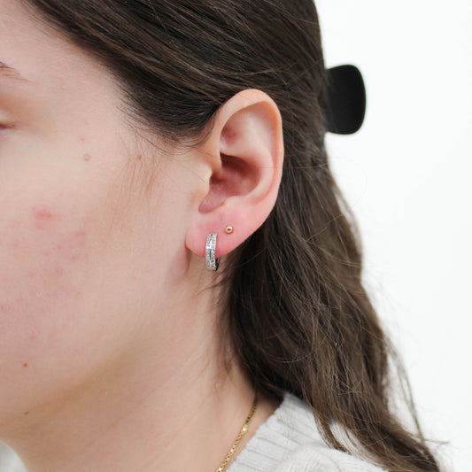 Close-up of a person wearing silver huggie hoop earrings with a plain background