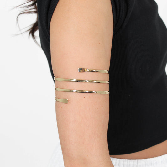 Gold layered arm cuff on a person's arm with a plain background