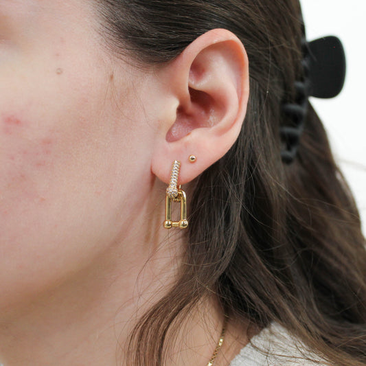 Close-up of a person wearing gold hoop link earrings with a blurred background