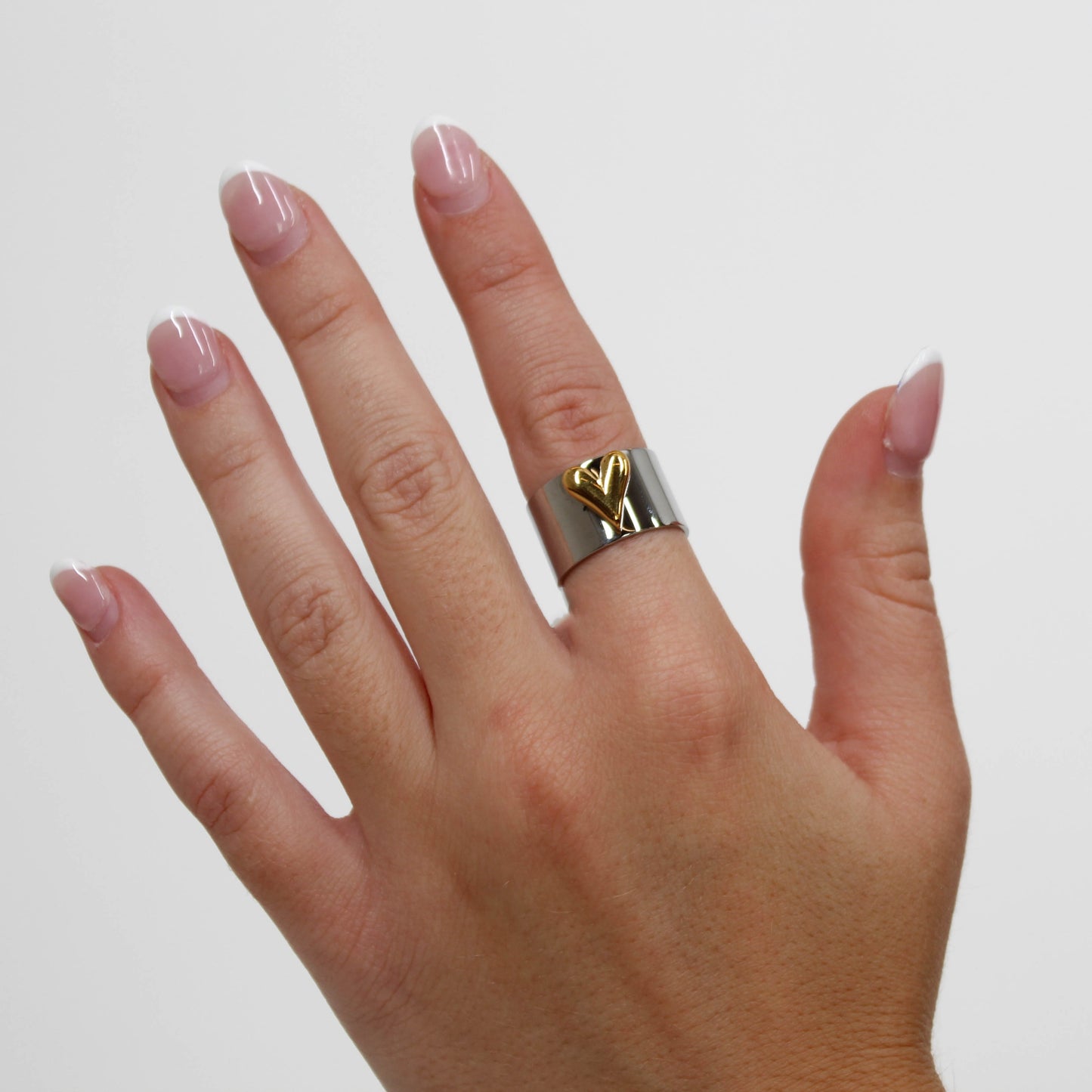 Hand wearing a silver ring with a gold heart design on a plain background