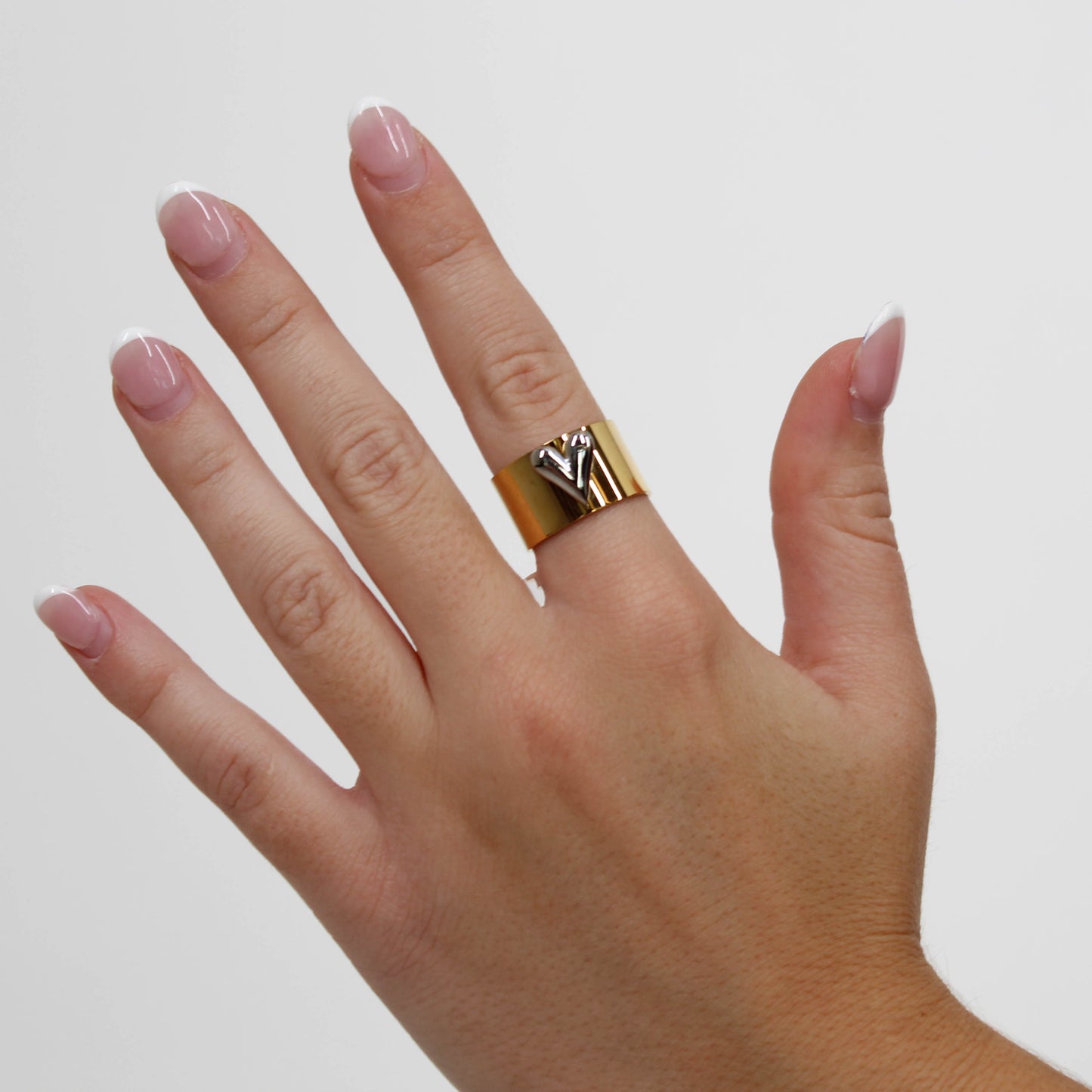 Hand wearing a gold ring with a silver heart on a plain background