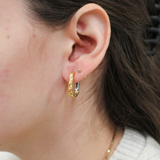 Close-up of an ear wearing mixed metal oval hoop earrings.