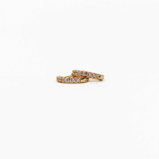 Two gold pave huggie earrings with diamond accents on a white background