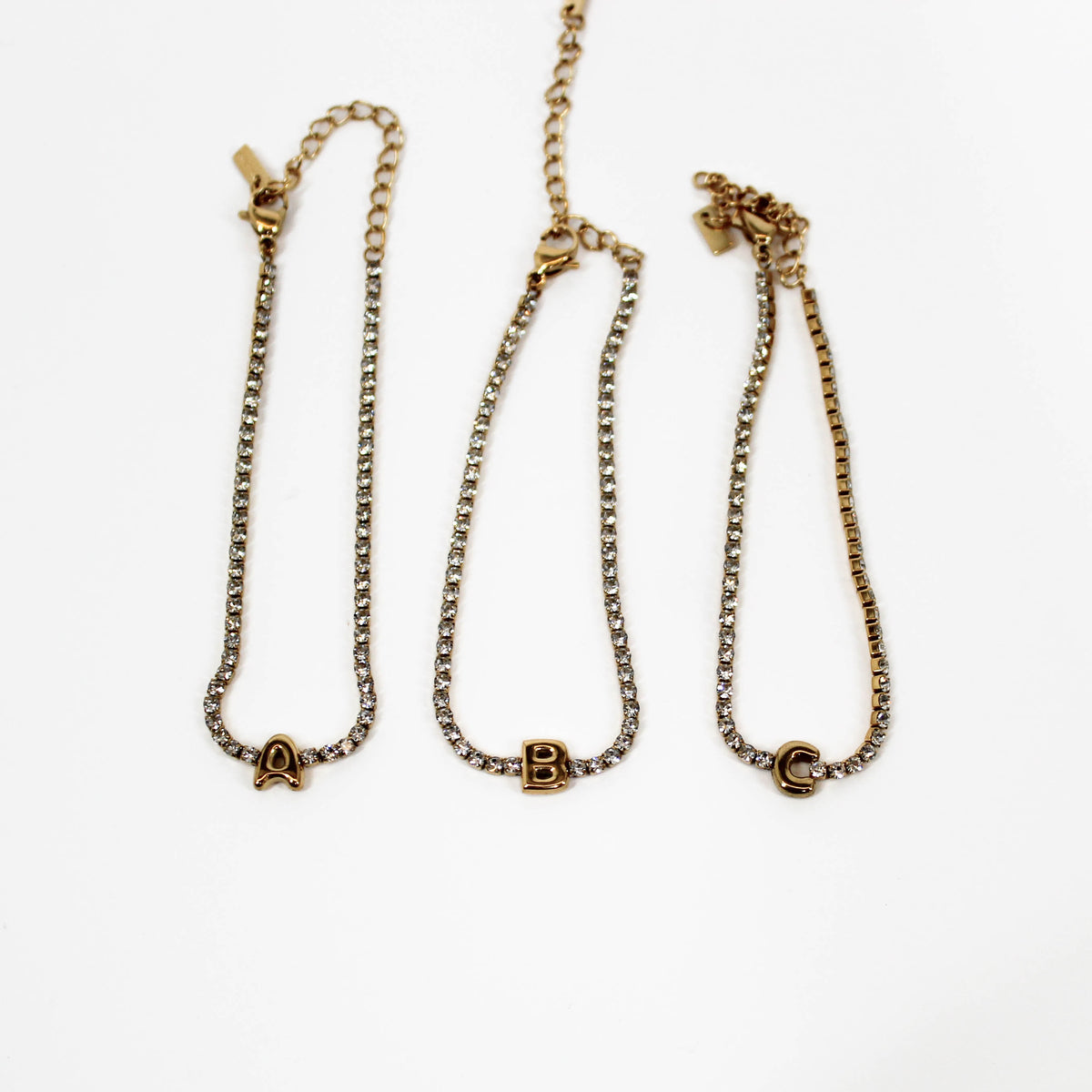 Three gold bracelets with letter pendants A,B,C on a white background