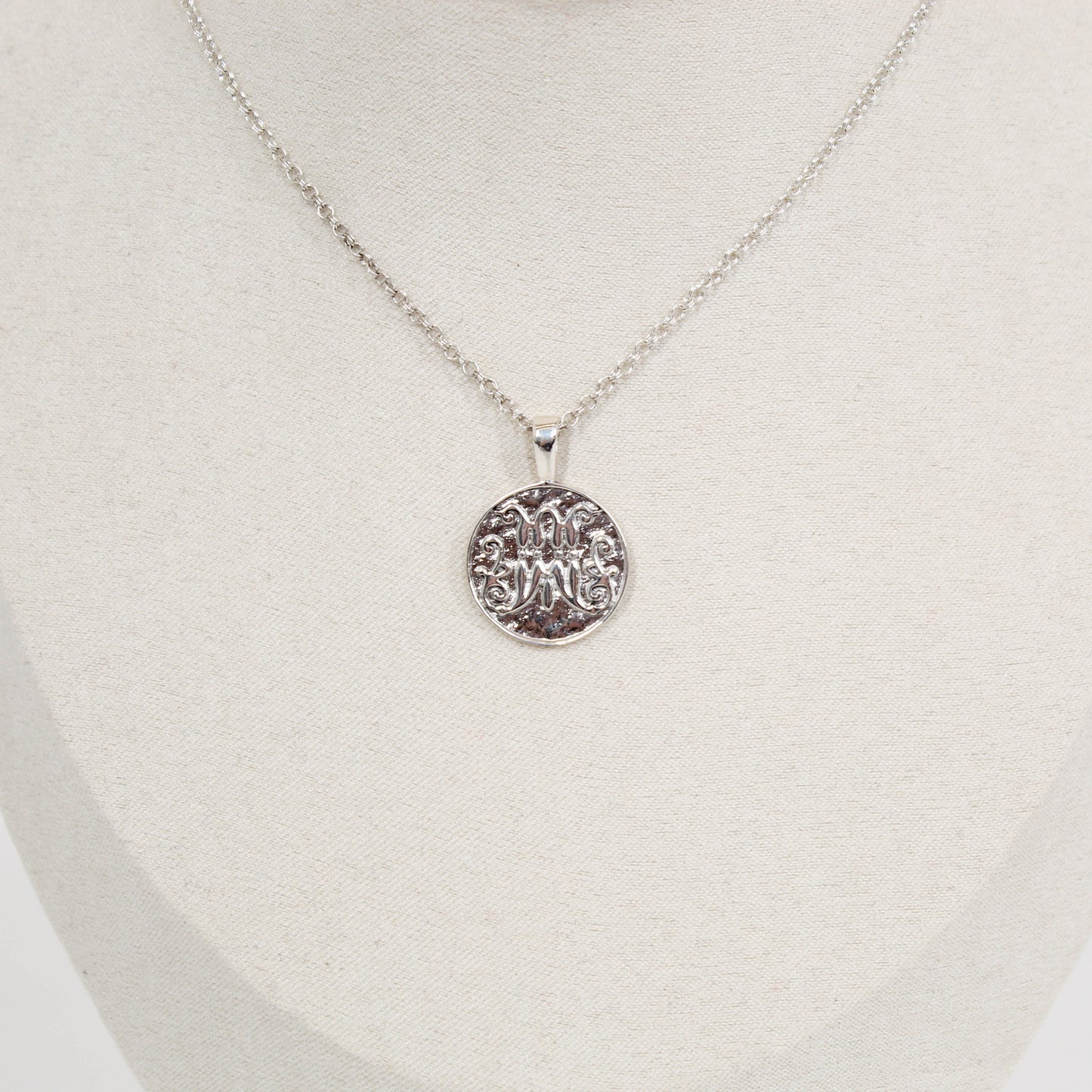 Silver scripted M Disc necklace for Marist on a white mannequin bust
