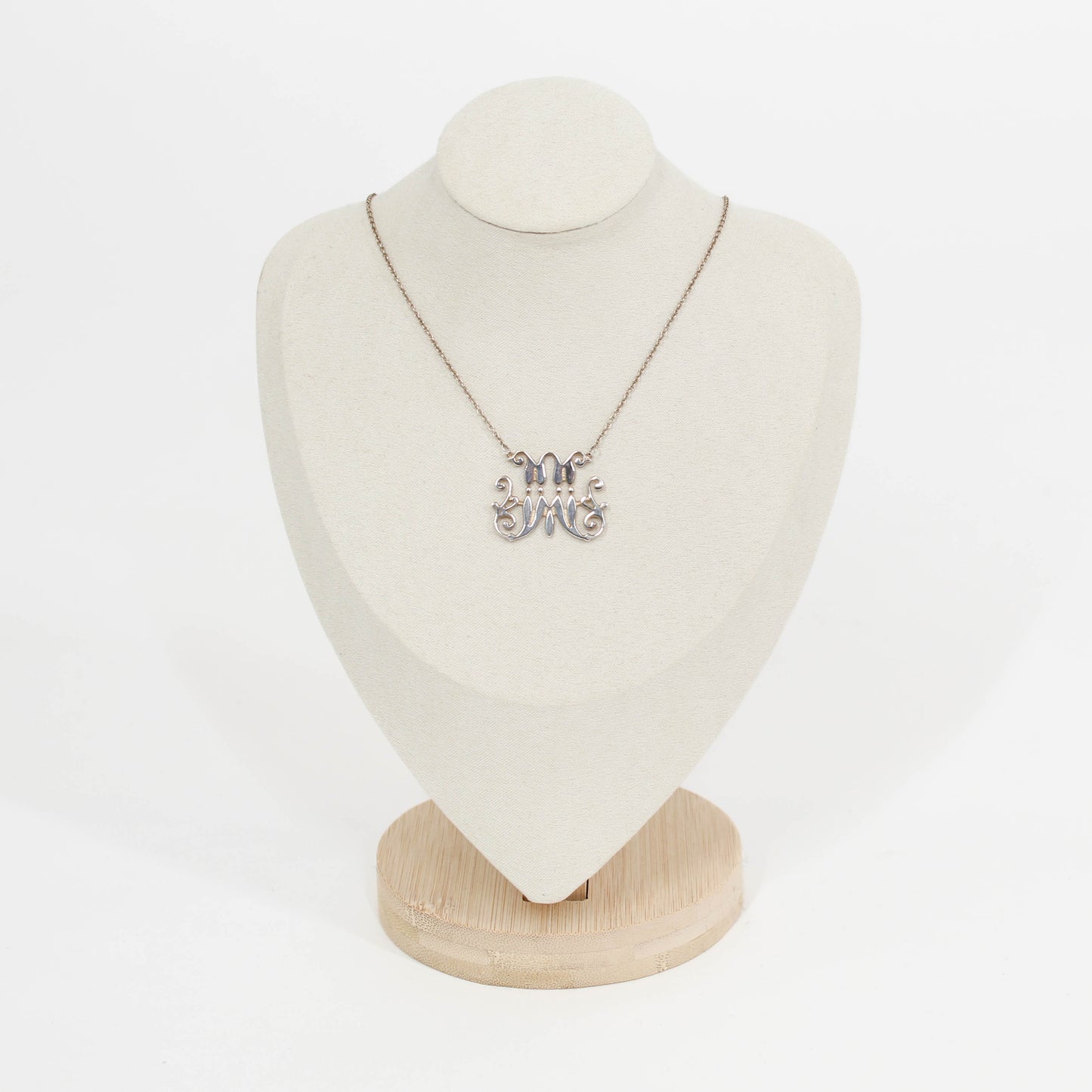 Necklace with a silver scripted M for Marist pendant on a mannequin bust against a white background