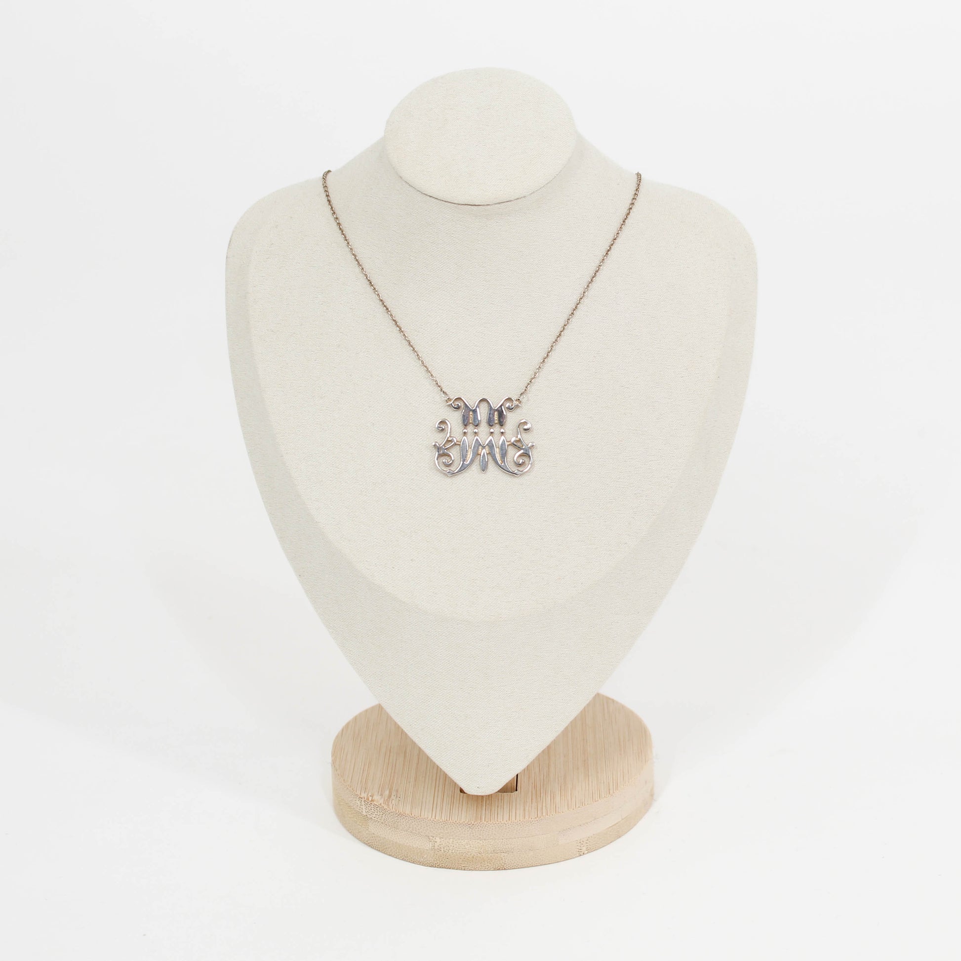 Necklace with a silver scripted M for Marist pendant on a mannequin bust against a white background