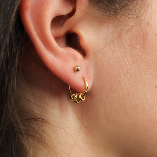 Close-up of a gold three ring hoop earring worn on an ear.