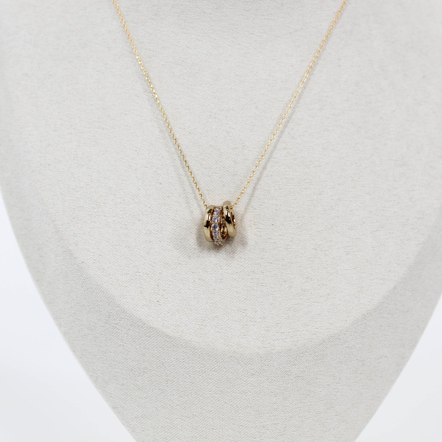 Gold three ring pendant necklace on a light gray stand