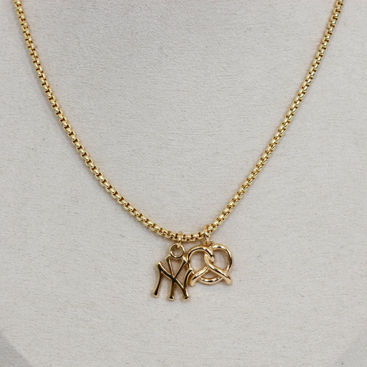 Gold yankee charm pendant necklace with a pretzel pendant on a light gray background
