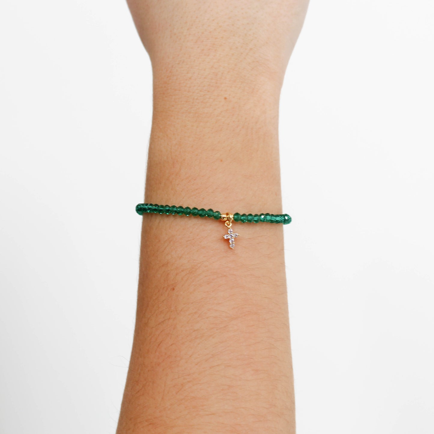 Emerald cross charm beaded bracelet with a cross charm on a wrist against a white background