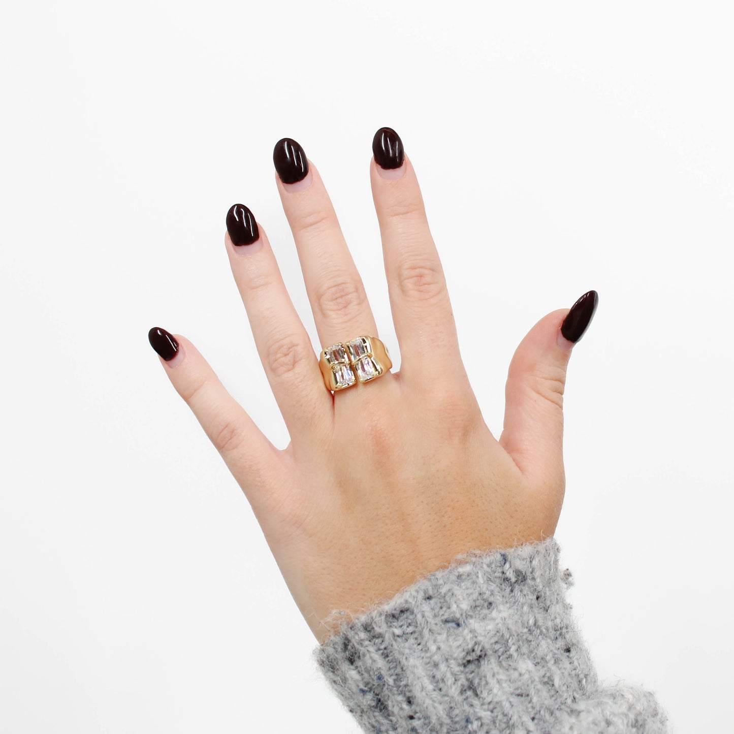 Hand wearing a gold baguette CZ signet ring with a clear stone on a white background