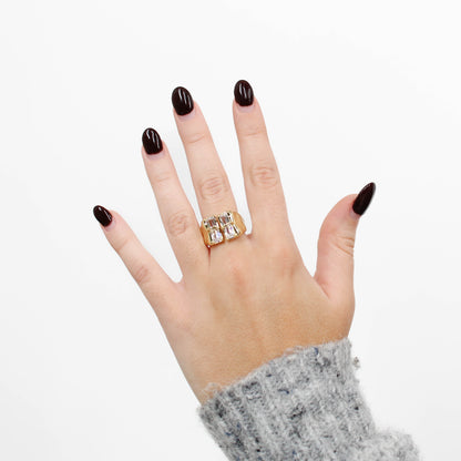 Hand wearing a gold baguette CZ signet ring with a clear stone on a white background