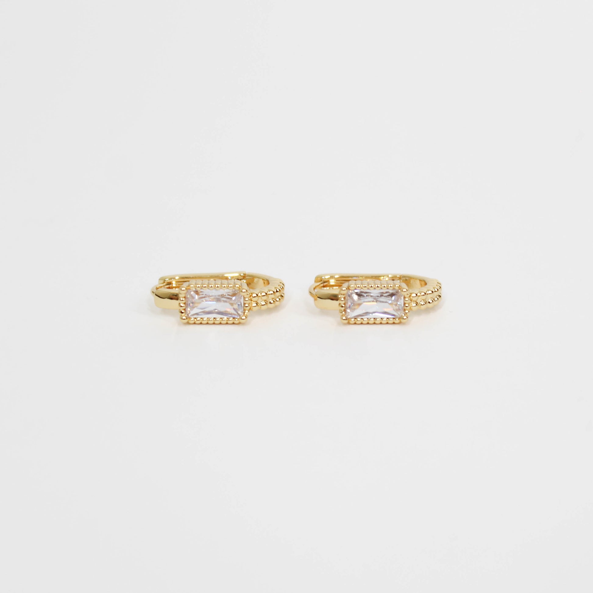 Gold hoop earrings with clear gemstones baguette oblong huggies on a white background
