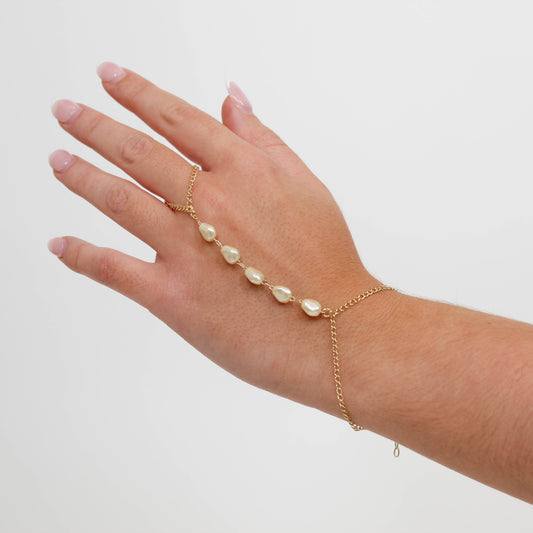 Hand wearing a gold pearl hand chain on a white background.