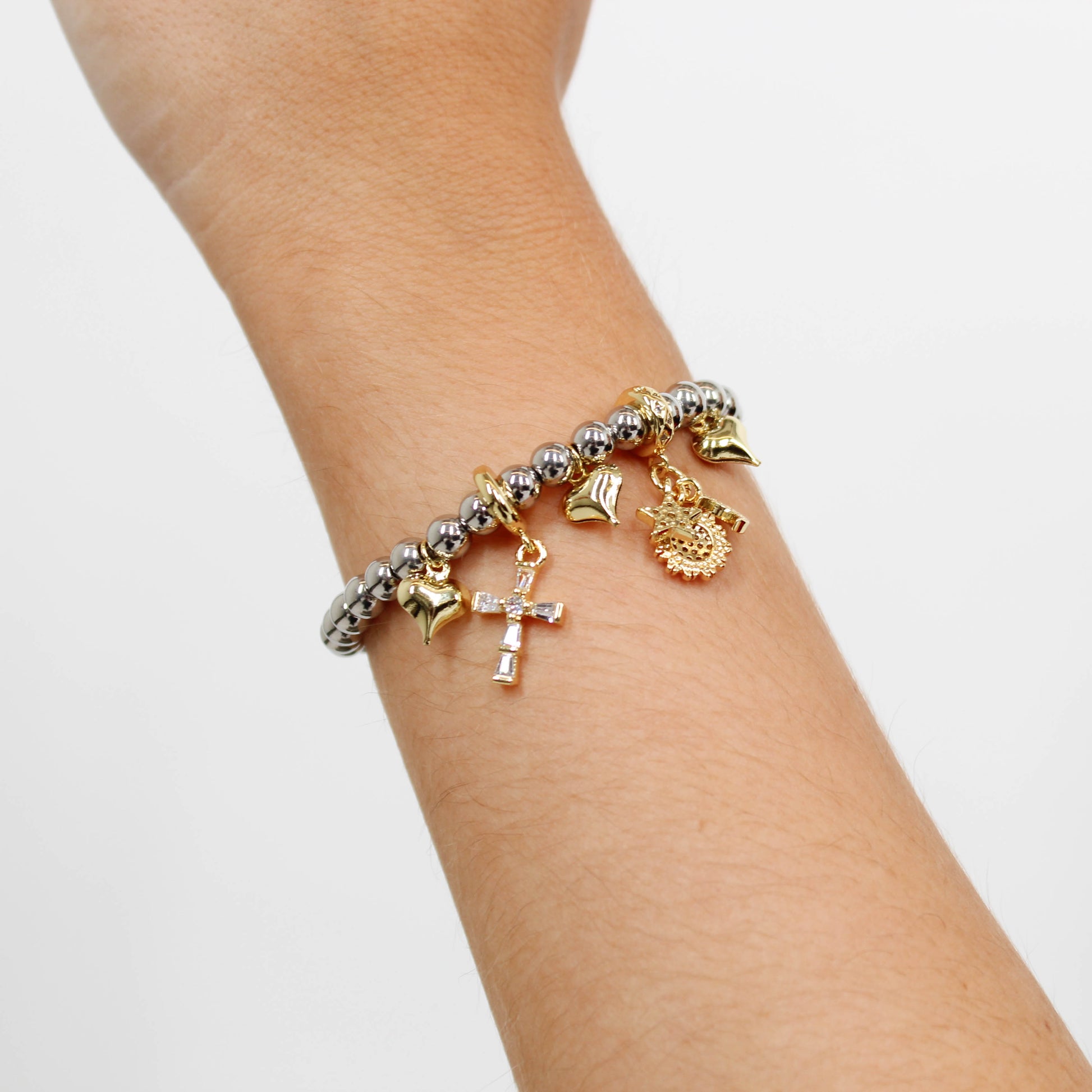 Beaded bracelet with various charms including a cross charm on a wrist against a white background