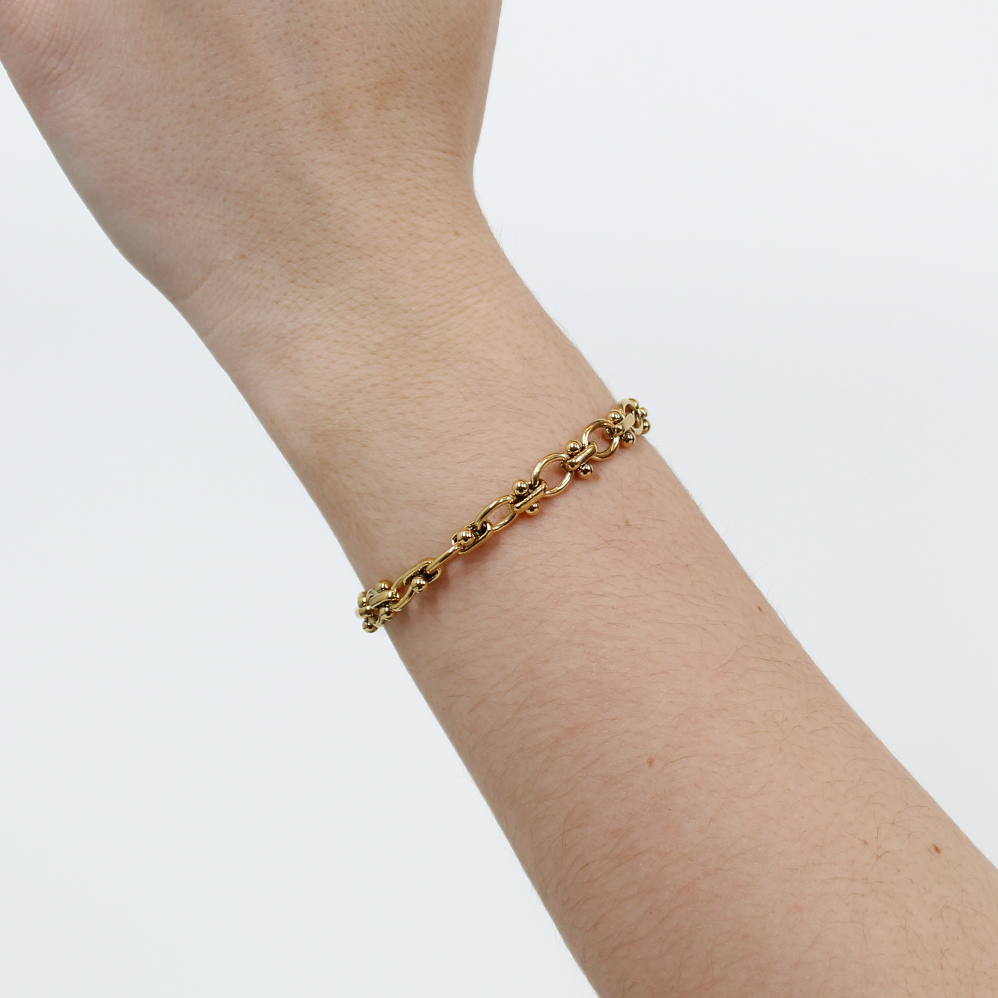 Gold beaded link chain bracelet on a person's wrist against a white background