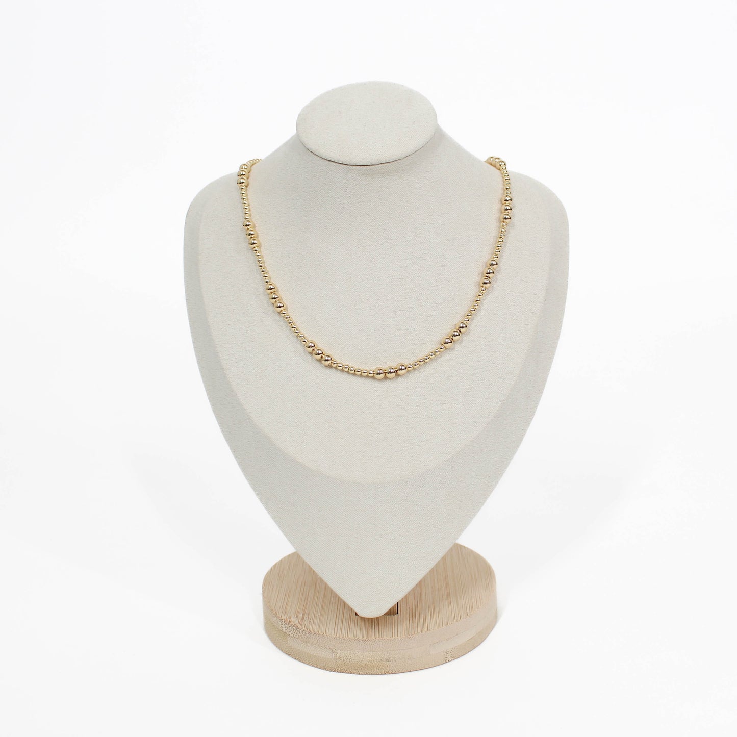 Gold necklace on a white bust with a wooden base against a white background