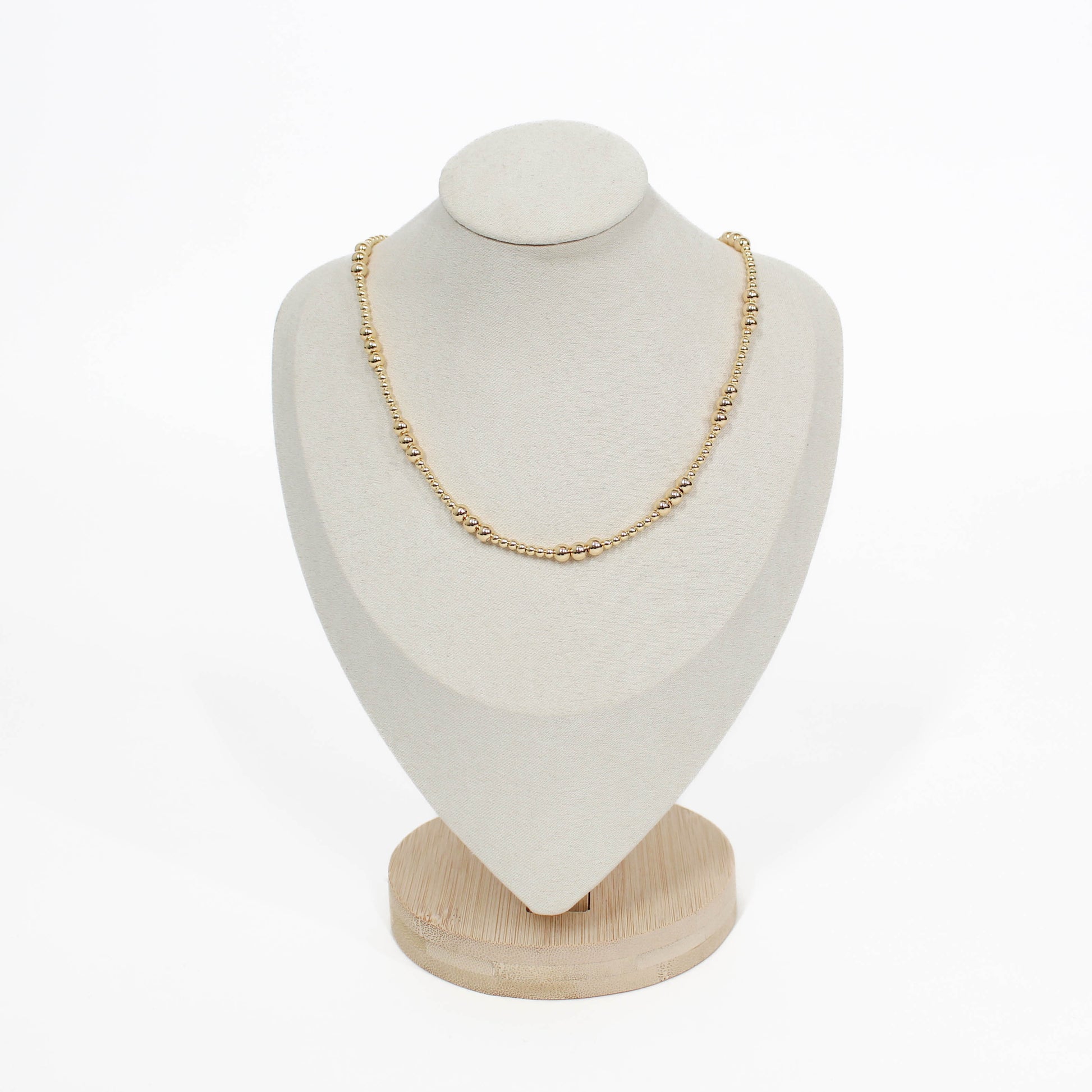 Gold necklace on a white bust with a wooden base against a white background