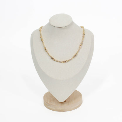 Gold necklace on a white bust with a wooden base against a white background