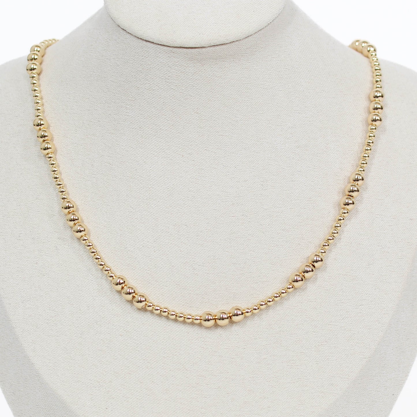Gold beaded necklace on a mannequin with a white background