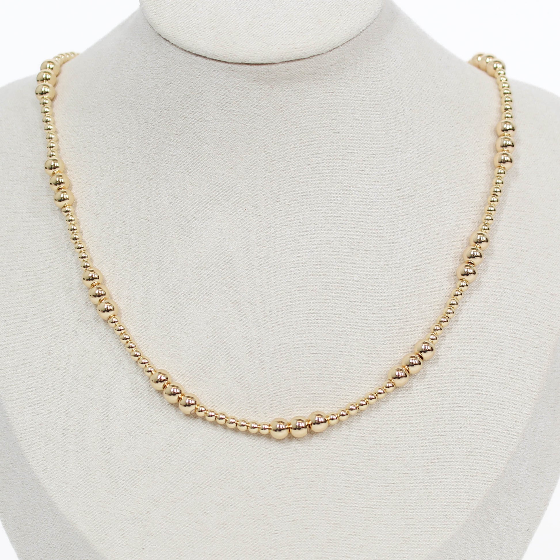 Gold beaded necklace on a mannequin with a white background