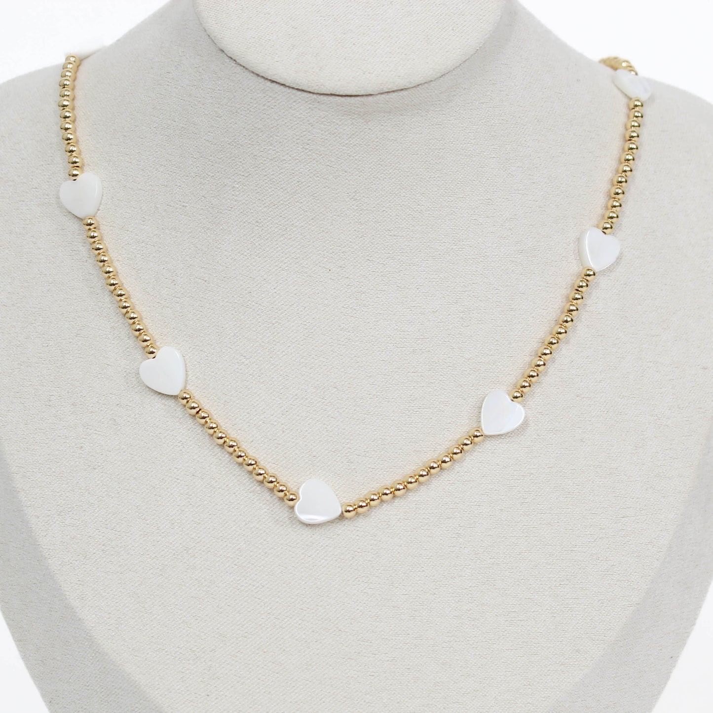 Gold chain beaded necklace with heart-shaped white pendants on a mannequin.