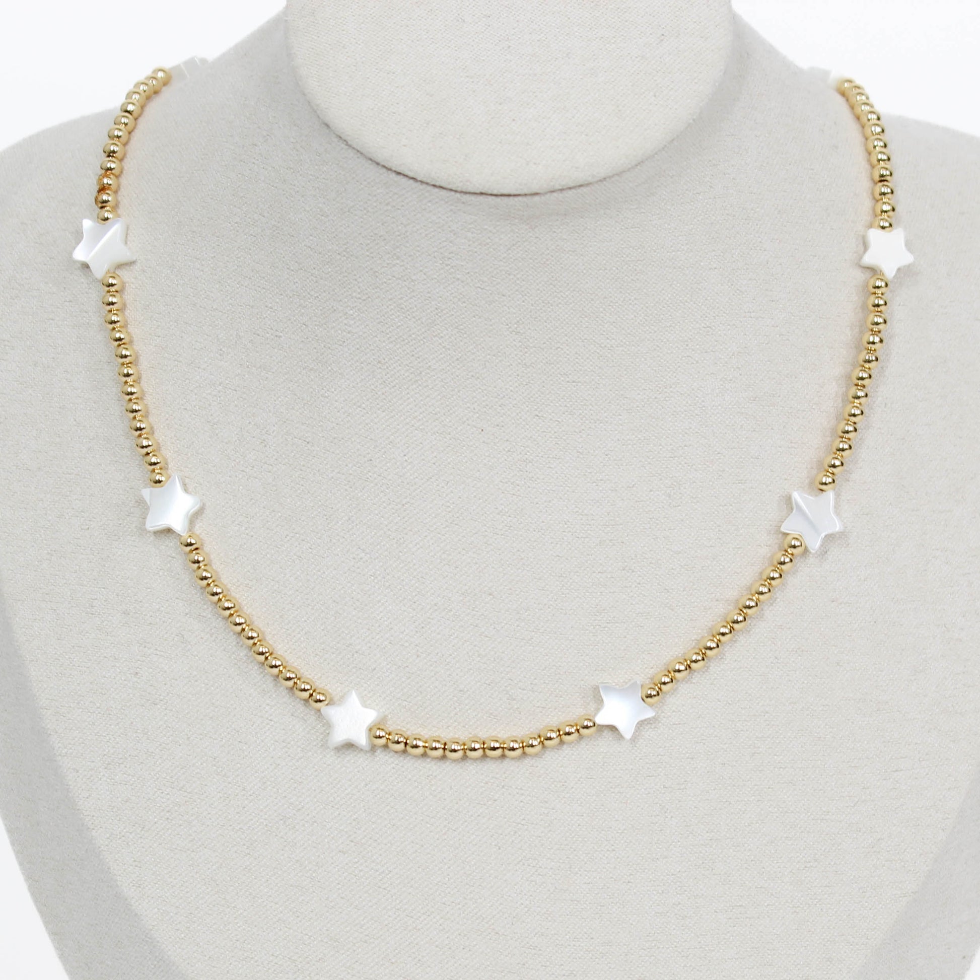 Gold beaded icon necklace with star-shaped pendants on a mannequin