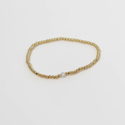 Gold beaded bracelet with a pearl on a light gray background