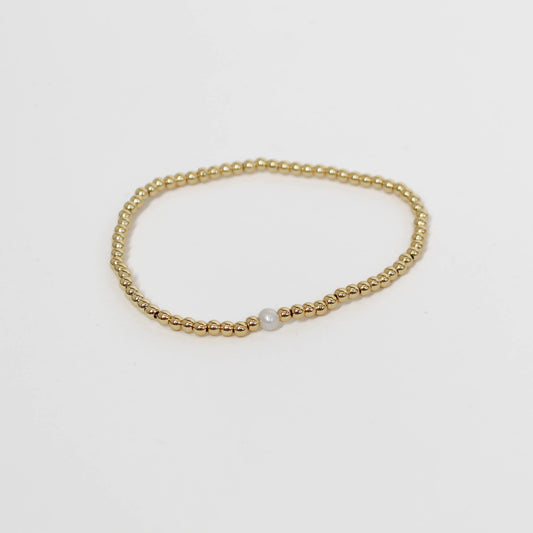 Gold beaded bracelet with a pearl on a light gray background