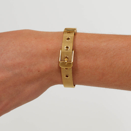 Gold belt bracelet on a wrist against a plain background