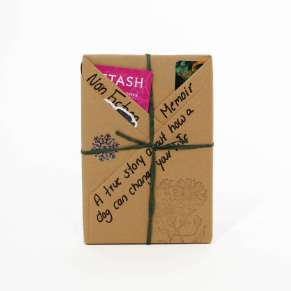 Book wrapped in brown paper with decorative text and a pink label on a white background