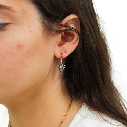 Close-up of a person wearing a silver heart-shaped bubble heart huggie earring.