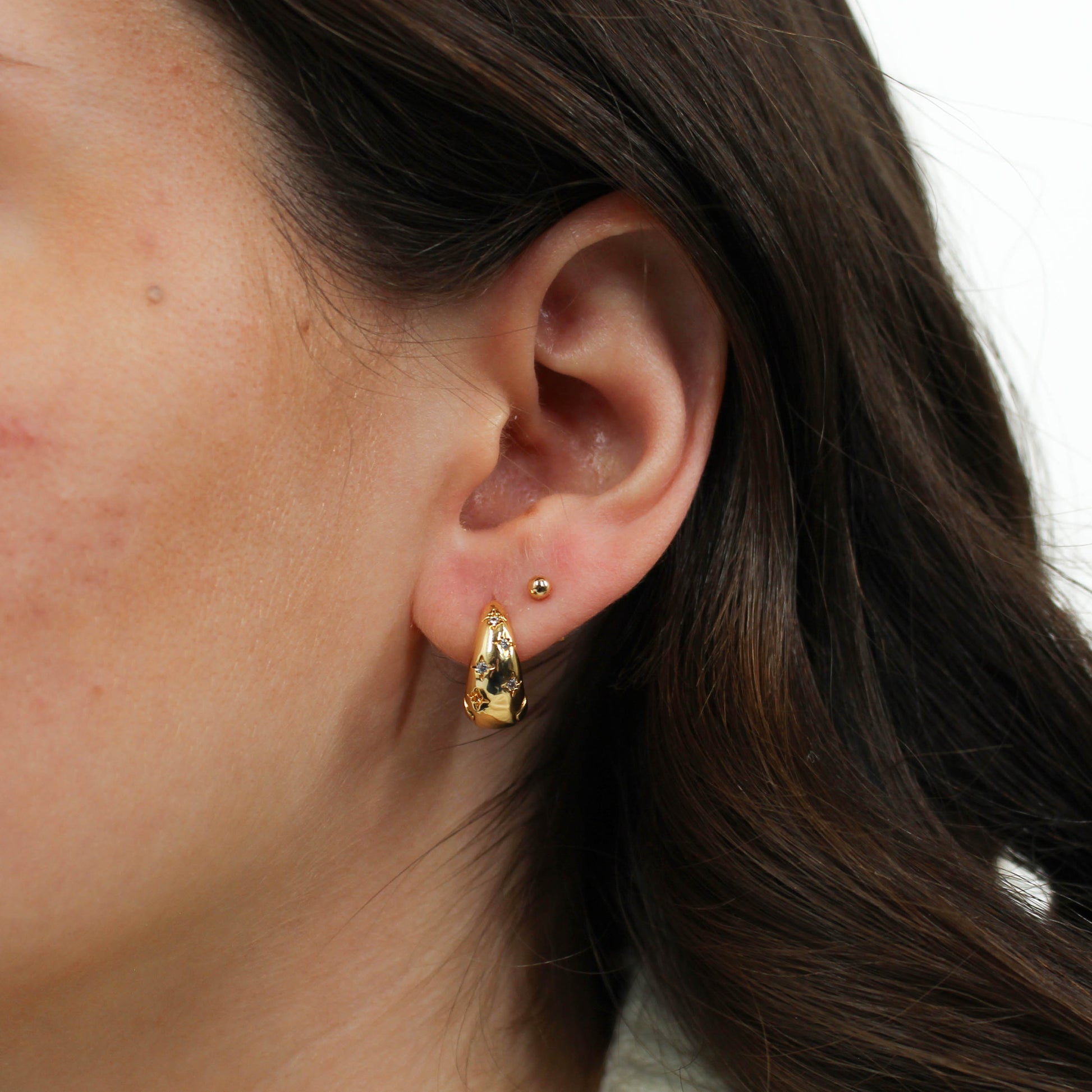 Close-up of an ear wearing gold hoop celestial star dome earrings