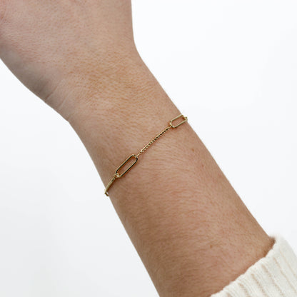 Gold chain link bracelet on a wrist with a white background