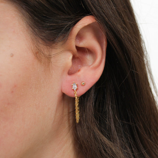 Close-up of an ear wearing chain link stud gold earrings with a plain background