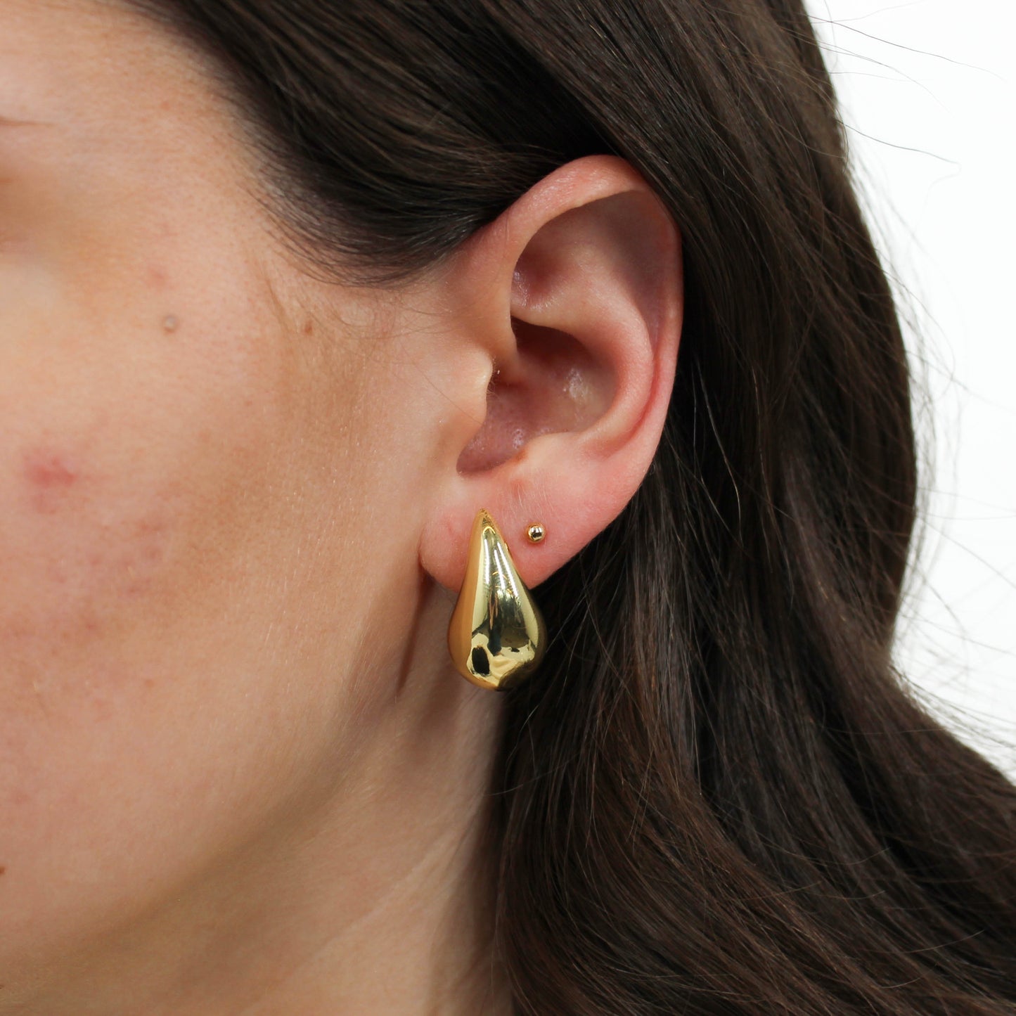 Close-up of a person wearing a gold chunky teardrop earring.
